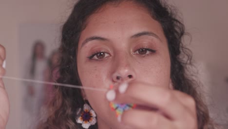 Closeup-of-woman´s-hands-and-brown-eyes,-making-crafts-with-colorful-little-beads,-needle-and-thread