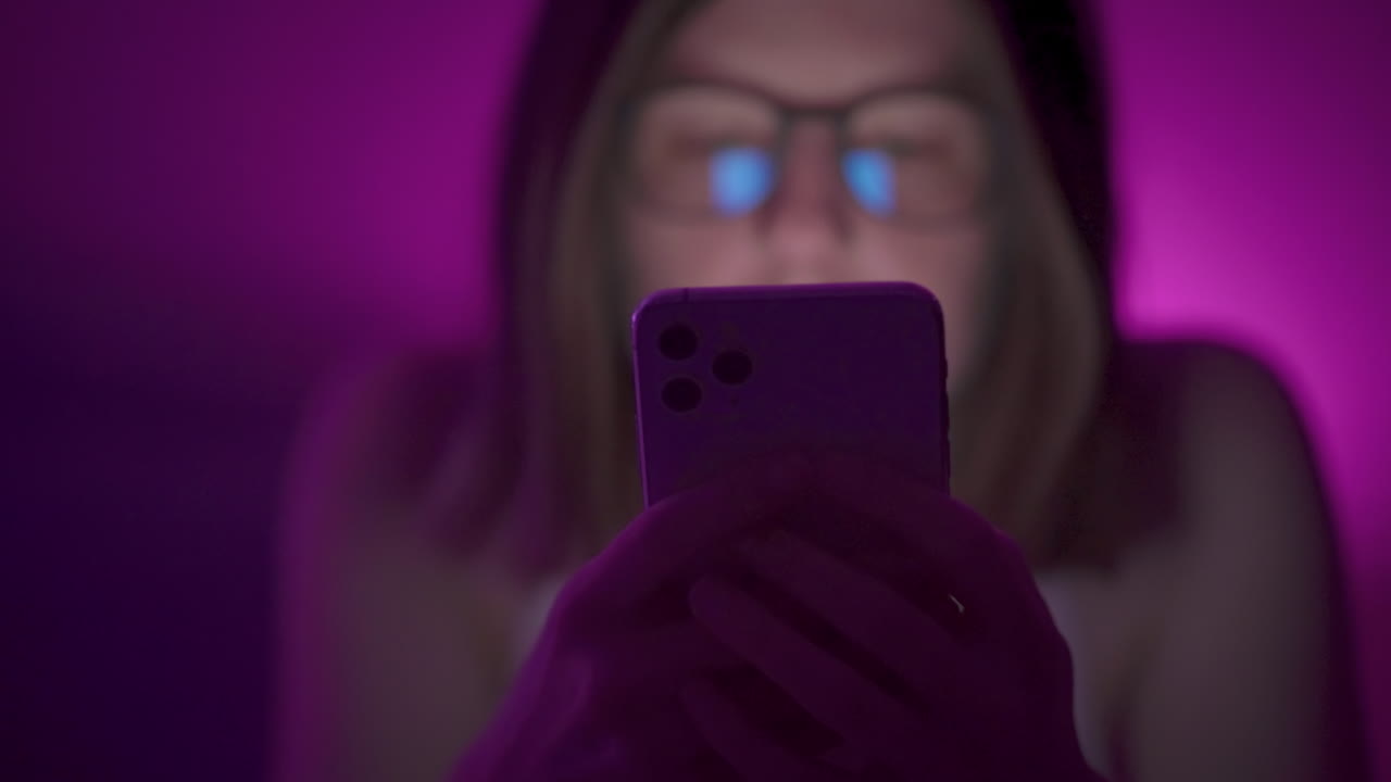 Silhouette of phone as girl browses social media on smart phone late at night in bedroom.