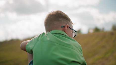 vista trasera de un niño con un corte de pelo elegante en la parte superior verde, mirando hacia el lado en vastas tierras de cultivo, la luz del sol suave destaca un paisaje rural pacífico con colinas onduladas y fondo borroso