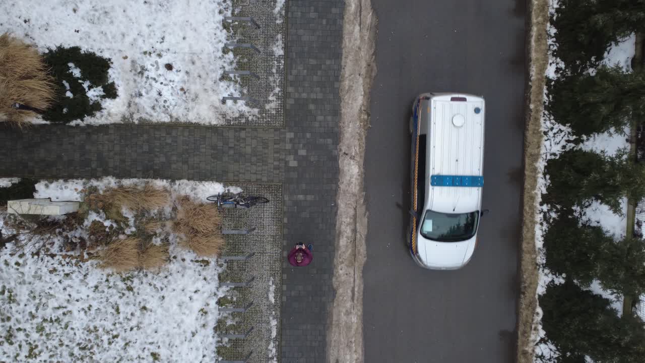 Vista aerea di un sentiero innevato con una donna, una bicicletta e un veicolo della polizia