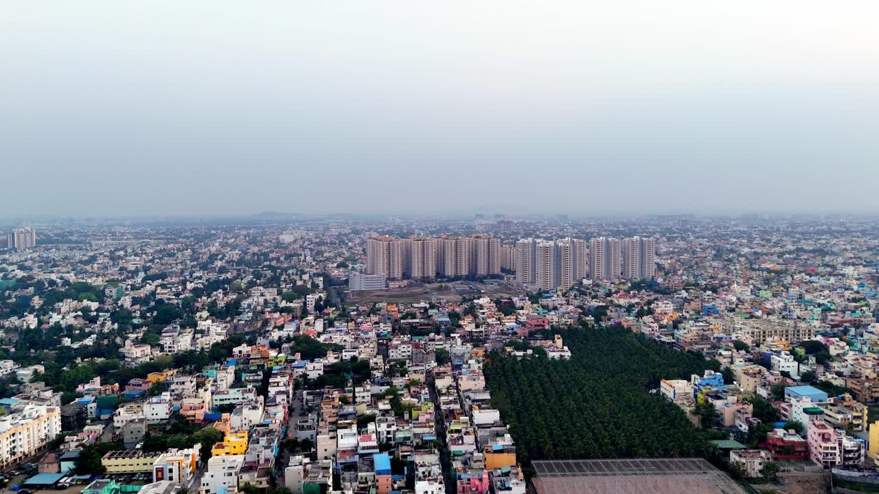 High-angle view of a bustling city. A modern high-rise building and a green patch sit within a dense urban tapestry. Excellent for showcasing urbanization and cityscapes