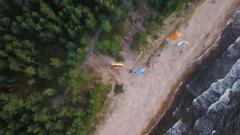 Aerial-top-down-view-of-tourists-enjoying-parasailing-on-sandy-beach-with-calm-waves-reaching-the-shore