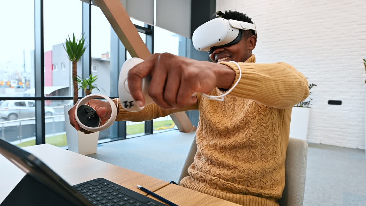 A black man exploring virtual reality using VR glasses and controllers in an office. Slow motion