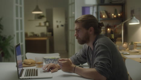 man using laptop and eating dinner