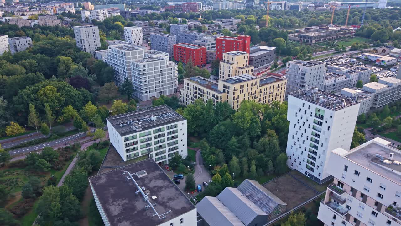 Arc drone shot over La Courrouze showing red buildings, passing bus and distant cranes in Rennes