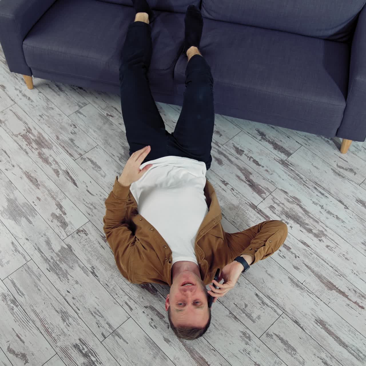 Young man speaking the phone at home. Tired man working through the phone while lying on a floor. Top view
