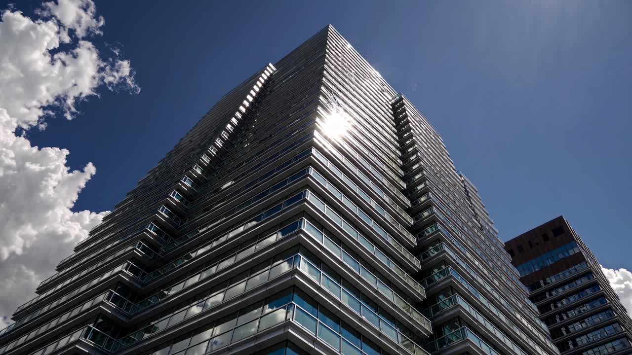 Low-angle video shot of a modern glass skyscraper reflecting sunlight, set against a bright blue sky