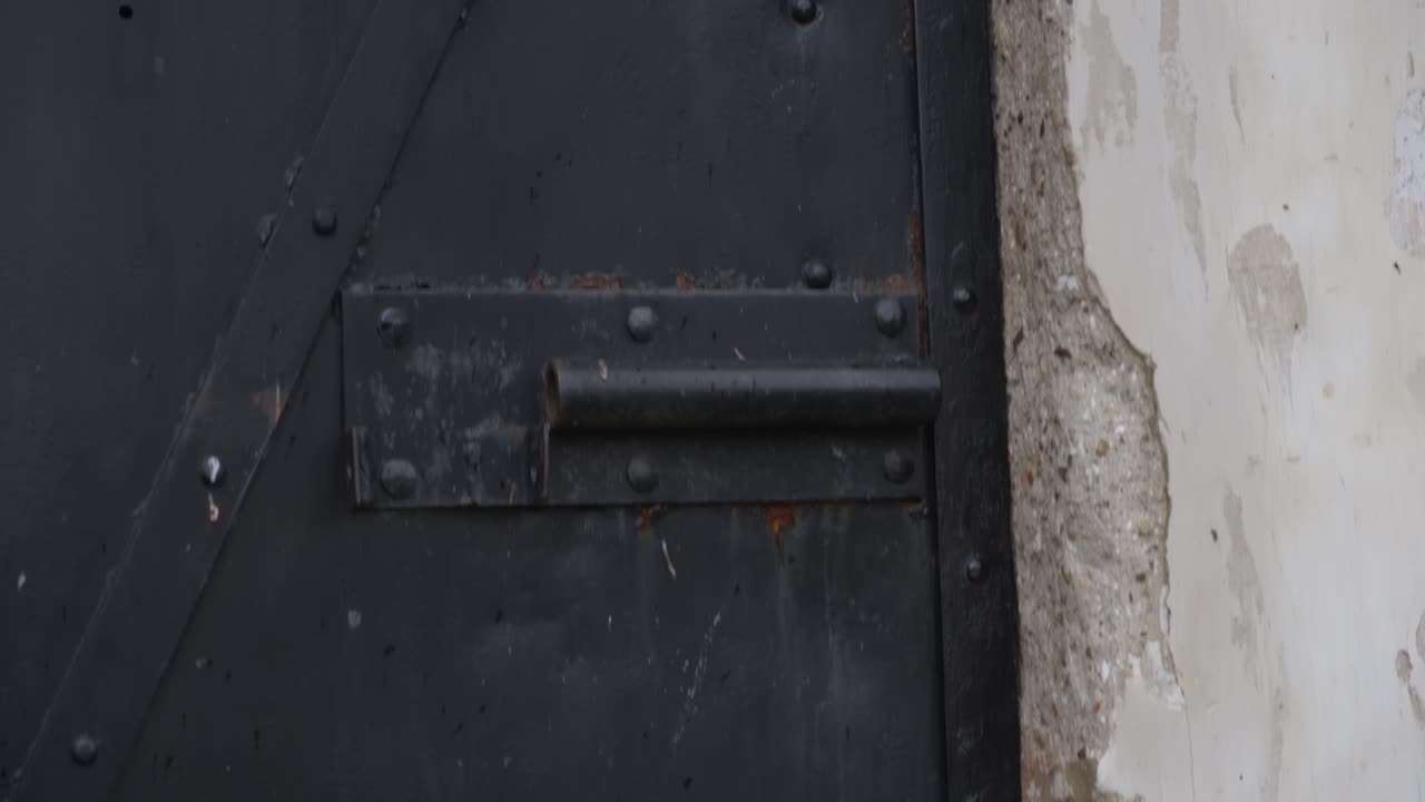 el movimiento lento de la cámara revela una vieja cerradura oxidada desgastada en una puerta de metal negro colocada en una vieja pared arañada