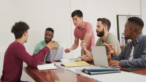 Happy-diverse-male-friends-talking-and-using-laptop-in-living-room