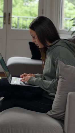 vertical video of anxious woman sitting indoors on sofa working from home using laptop worried about cost of living crisis