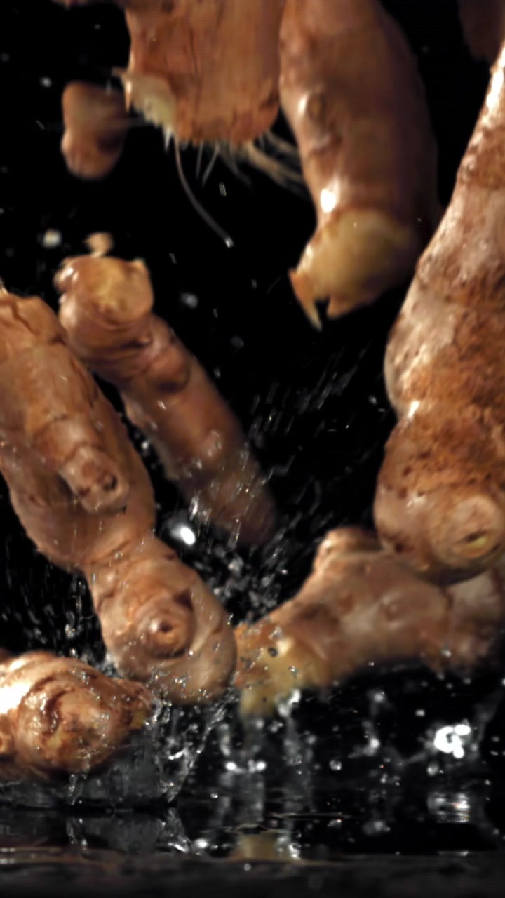Radici di zenzero fresche che cadono e schizzano nell'acqua al rallentatore