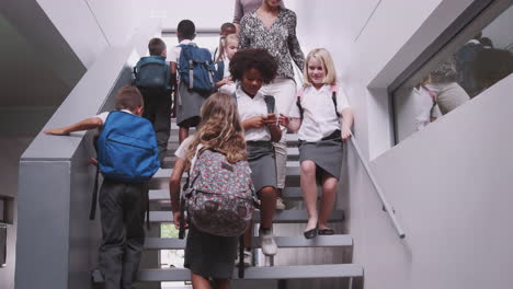 teacher and pupils walking down stairs in busy elementary school corridor