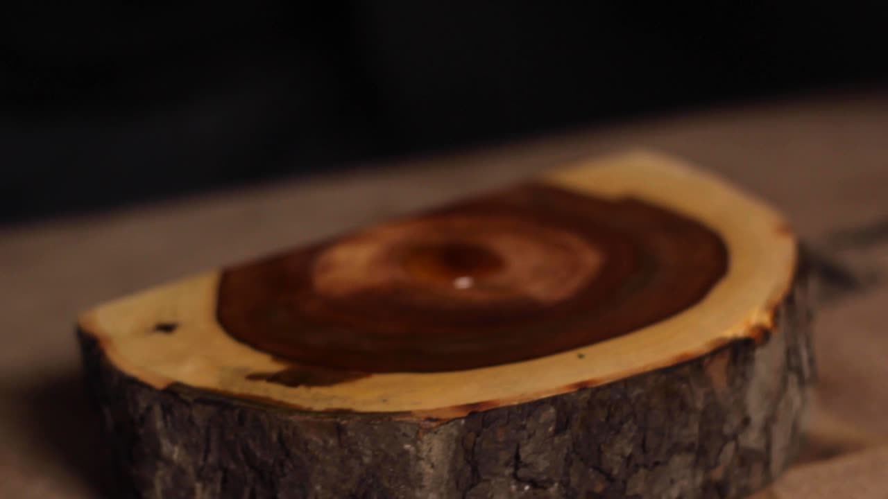 Close up of hands staining and polishing a sliced piece of tree log on a flat surface, making it smooth and shiny
