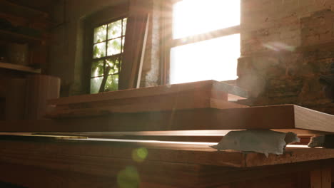 sunlight filters into a workshop, highlighting wooden boards on a workbench. tools lie nearby as a craftsman engages in woodworking, creating something unique in the afternoon light.
