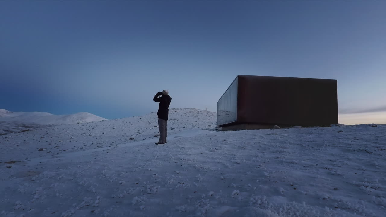 집 밖의 눈 덮인 풍경에서 먼 풍경을 보는 쌍안경을 가진 남자
