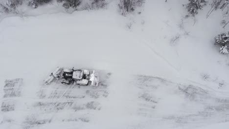 a tractor navigating a snow-covered country road bordered by dense coniferous trees - aerial drone shot