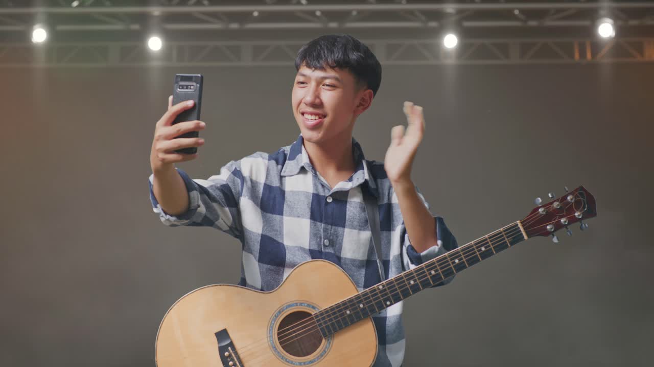 기타를 흔들고 무대에 서서 스마트폰으로 비디오 통화를 하는 아시아 십대