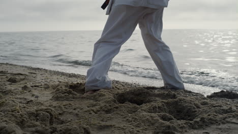 unknown man legs making karate kicks on sand close up. athlete stepping on beach