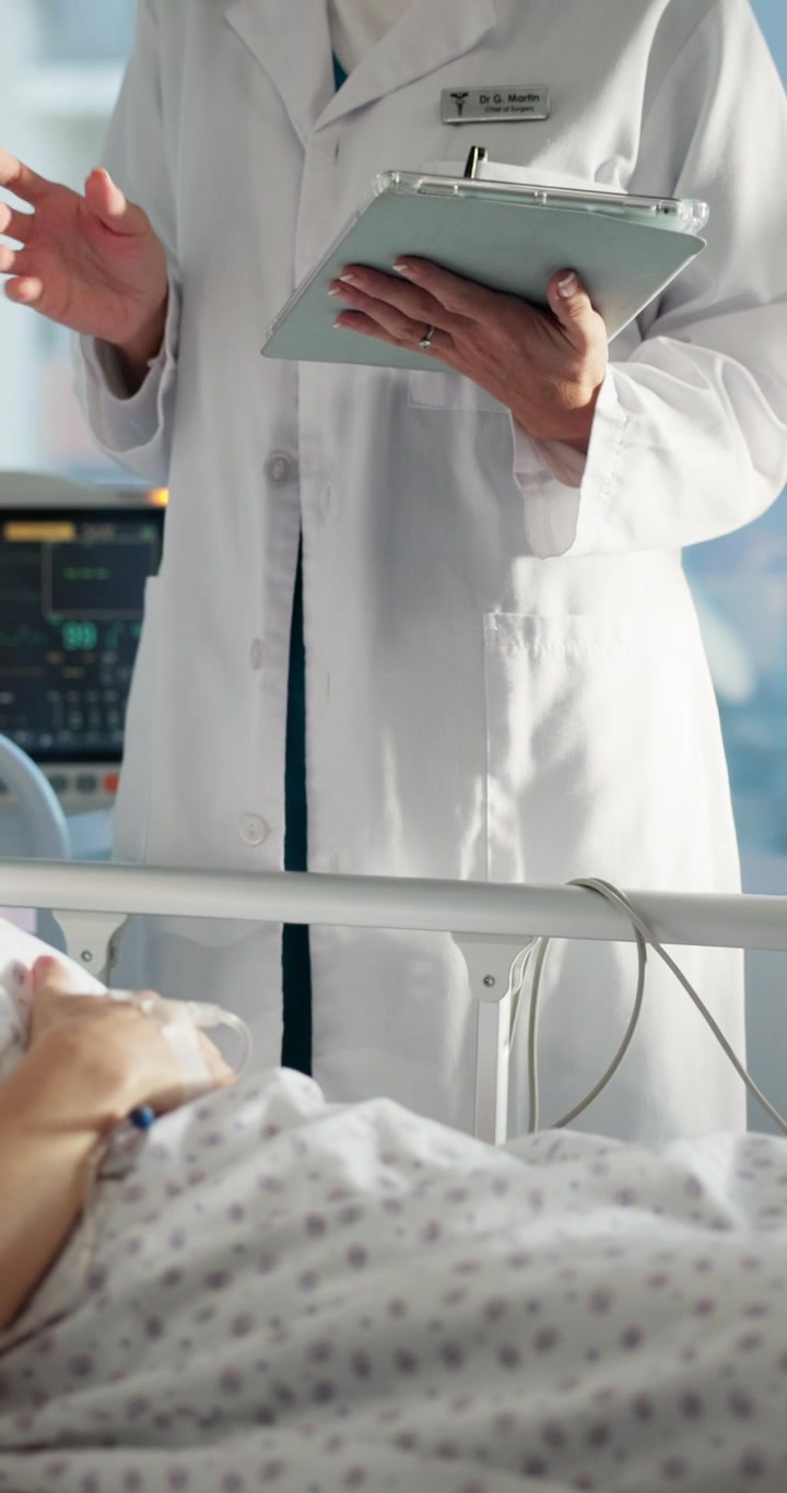 Læge diskuterer medicinsk rapport med patient på hospitalsstue