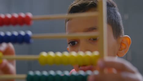 Front-view-of-Asian-schoolboy-solving-math-problem-with-abacus-at-desk-in-a-classroom-at-school-4k