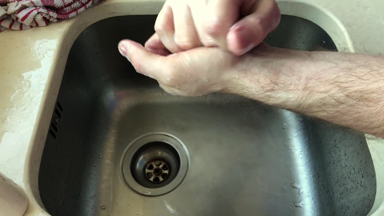 Medium shot of adult male cleaning hands using soap at sink, no face