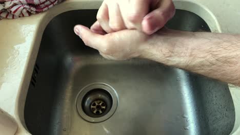 medium shot of adult male cleaning hands using soap at sink, no face