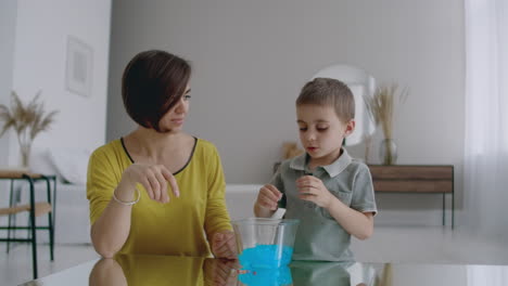 in a white apartment sitting on the floor mom and boy used to play a stretchable plasticine toy laughing and smiling together.