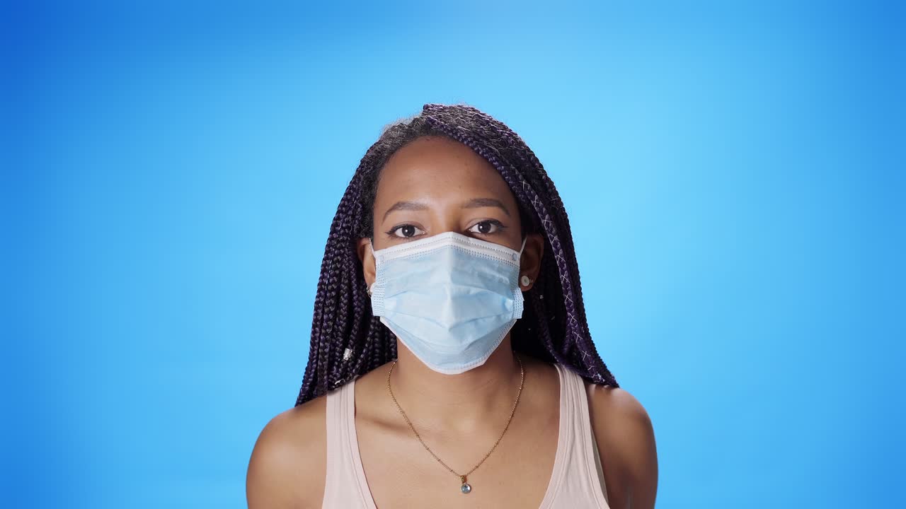 Portrait of a smiling black African American woman looking at the camera putting on a mask on a blue background. New normal in times of coronavirus due to covid19 pandemic.