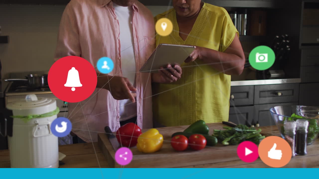 red de iconos digitales contra una pareja mayor que usa tableta digital en la cocina en casa
