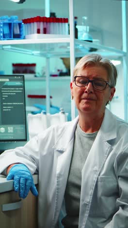 vertical video: portrait of old chemist woman with fatigued face in front of camera