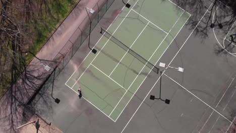 drone footage looking straight down while flying up over basketball and tennis courts with someone skateboarding and another person playing basketball with shadows