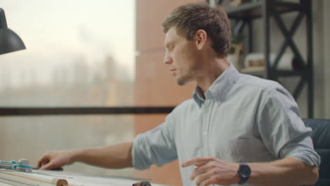 Architect-man-sits-at-drafting-table-in-modern-industrial-office-during-the-day.-Architect-working-on-blueprint-with-spesial-tools-and-pencil-close-up.-Male-architect-at-work-only-hands-with-ruler-and-pencil.-Design-of-the-house.-Engineer.-Tools-for-drawing.-Creating-a-drawing.