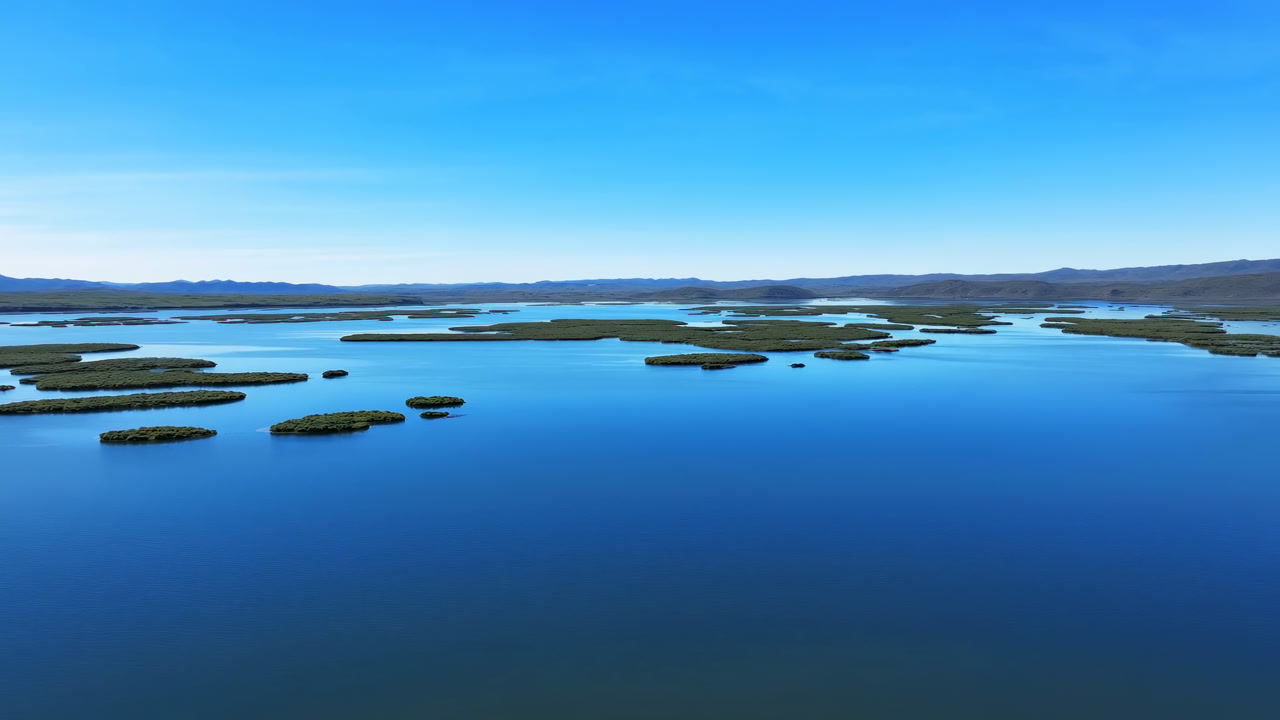Aerial Island Archipelago Over Calm Water, Clear Blue Sky, Distant Low Mountains, Scattered Vegetated Islets