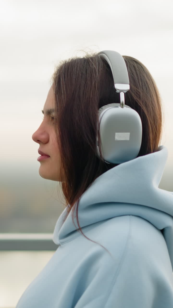 Close-up side view of woman in hoodie and headphones walking gently, blinking eyes, peaceful walk by river, calm outdoor setting with blurred river view in background, tranquil atmosphere