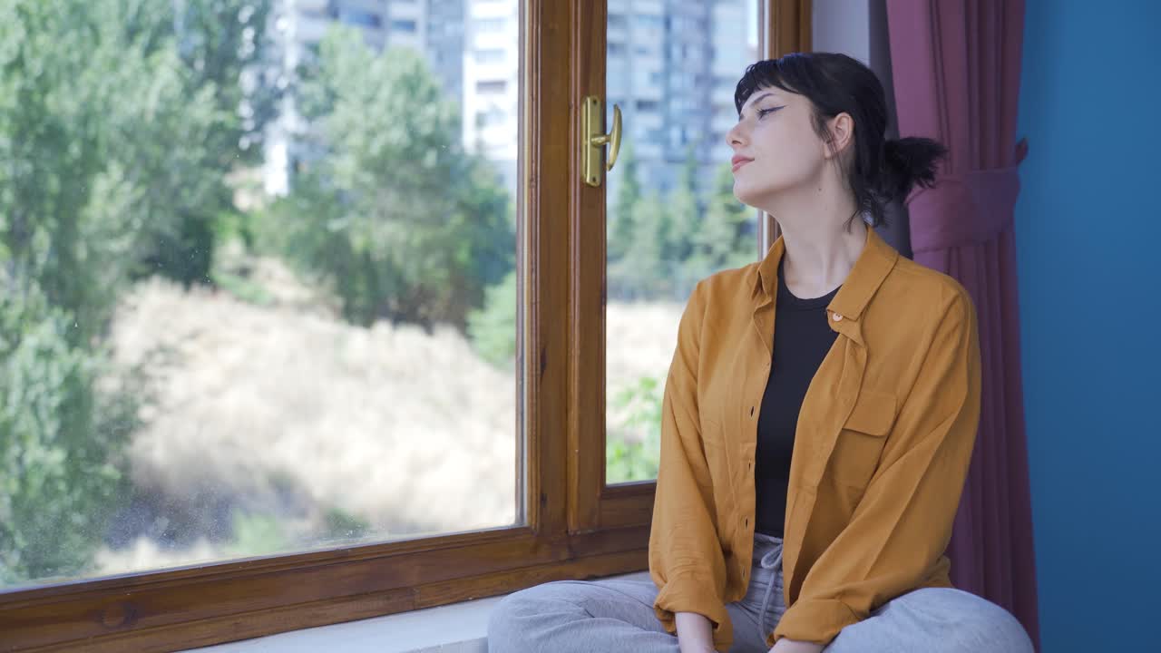 La giovane donna davanti alla finestra, che fa un respiro profondo e chiude gli occhi