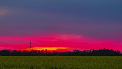 Dramatischer-Sonnenuntergang-Durch-Farbenfrohen-Himmel-Mit-Grünem-Feld-Im-Vordergrund,-Zeitraffer