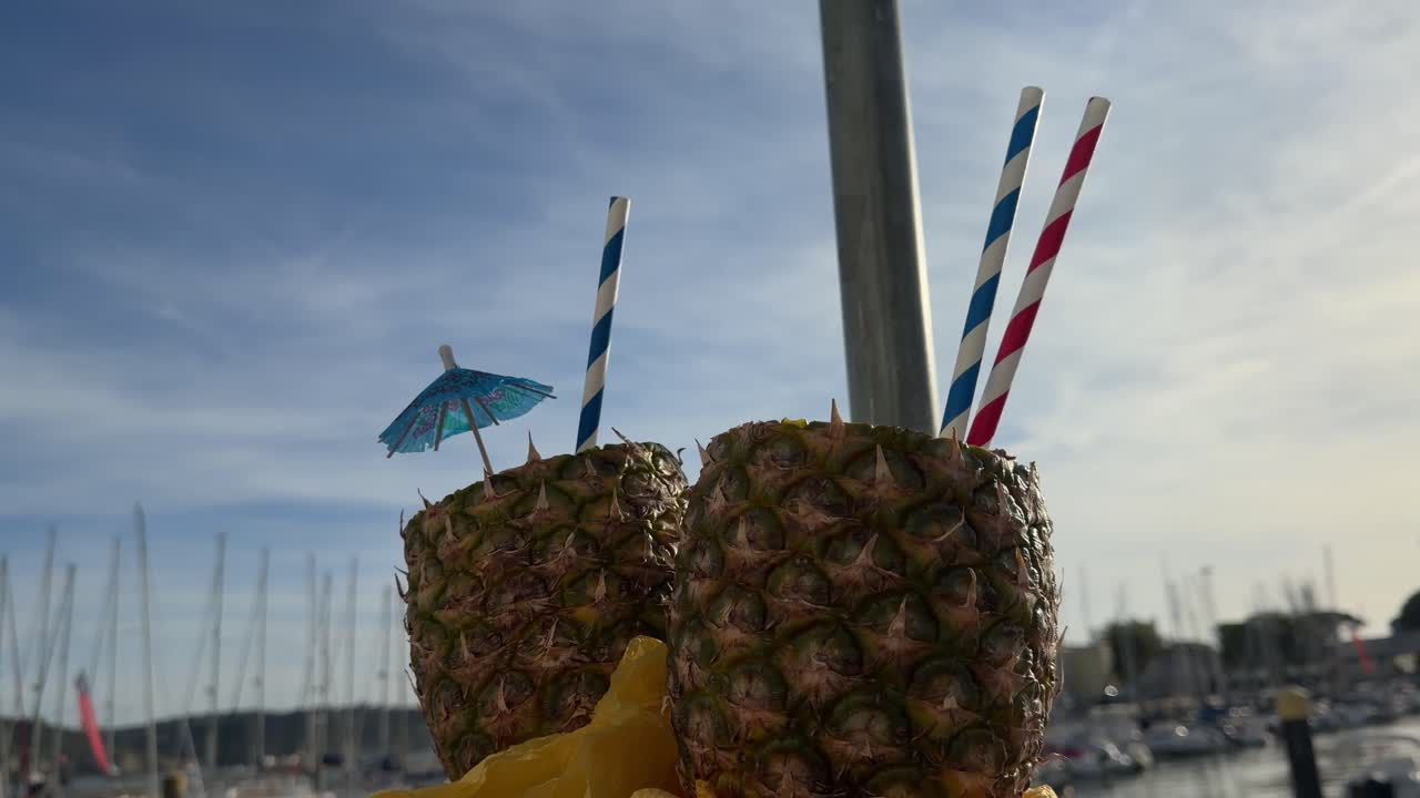 Due bevande tropicali all'ananas con cannucce in una marina soleggiata.