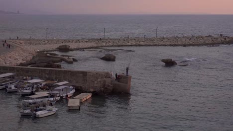 Boats-moored-near-stone-wall-in-old-port-at-sundown