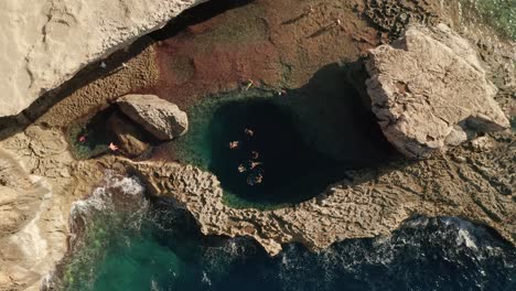 Vista-Aérea-De-Personas-Nadando-En-Un-Mar-Azul-Prístino-En-El-Famoso-Agujero-Azul-En-Dwerja-En-La-Isla-De-Gozo,-Malta