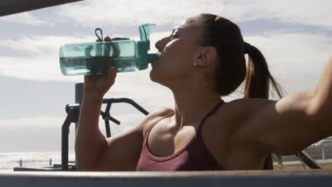 sporty caucasian woman drinking water in an outdoor gym during daytime