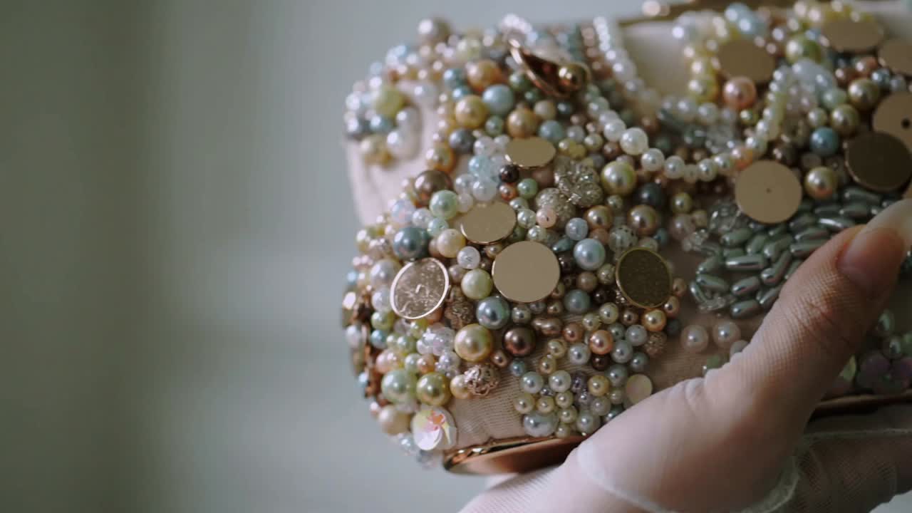 Holding gloved hand sliding manicured finger across beaded clutch in soft lit room showing pearls
