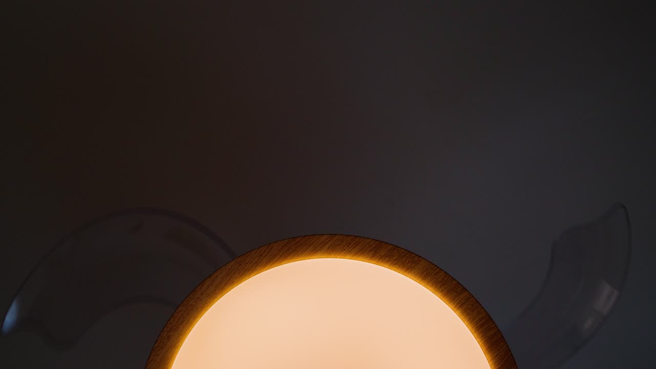 Plafoniera con pale di ventilatore rotanti che proietta ombre tenui su una parete poco illuminata.