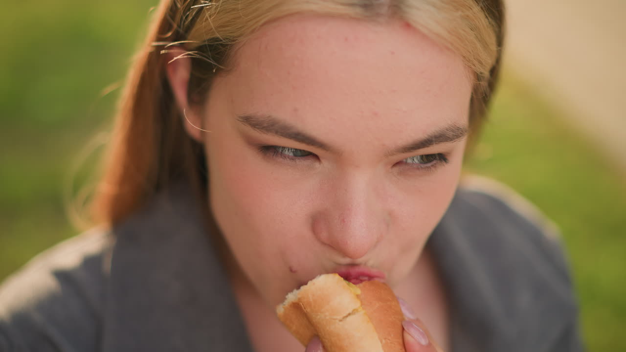 primer plano de una dama disfrutando de shawarma al aire libre, centrándose en su mano sosteniendo el bocadillo y el momento de comer, fondo verde borroso con suave luz del día