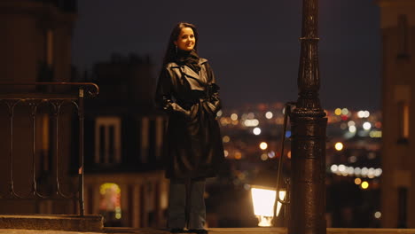 Brunette-Model-Woman-Standing-Alone-Outside-in-Paris-City-By-Night,-Dressed-in-Black-Coat