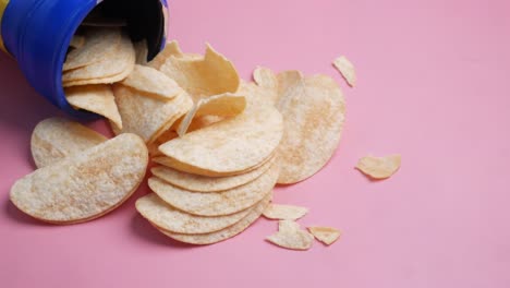 chips derramándose de un recipiente azul en un fondo rosado