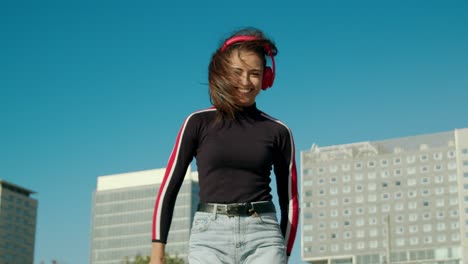 zoom in of an empowered happy young attractive latin woman enjoy dancing listening to music with wireless red headphones at the city