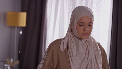 muslim woman wearing hijab at home standing and praying 4