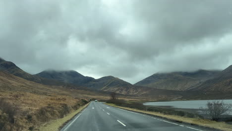 a car drives through the moody scottish highlands on an overcast day, with cloud-covered hilltops creating a serene, misty landscape full of wild, untamed beauty and quiet solitude.