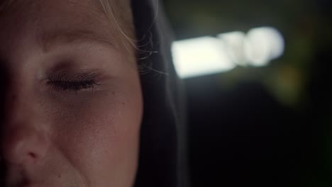 blonde woman close blue eyes at night, white light background, closeup