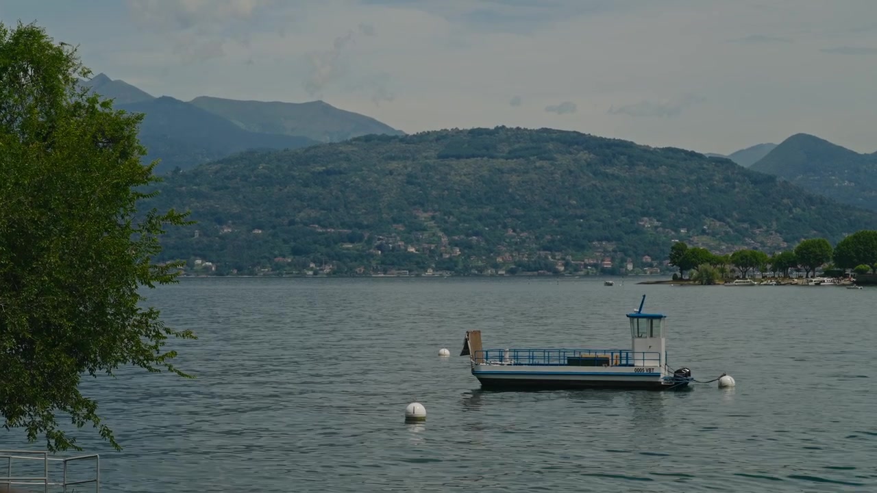Un piccolo traghetto passeggeri riposa pacificamente su un lago calmo circondato da maestose montagne alpine, catturando acque tranquille, bellezza paesaggistica e il fascino del nord Italia.